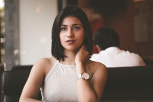 Woman wearing a gray spaghetti strap shirt while seated at a restaurant.