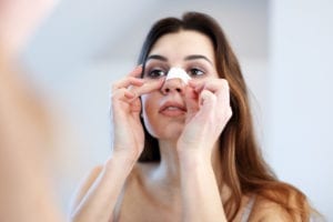 Woman adjusting her nose bandage as she recovers from rhinoplasty.