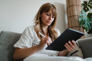 Woman sitting on her couch working on her tablet.