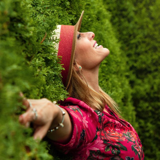 Woman leaning into tall hedge looking up.